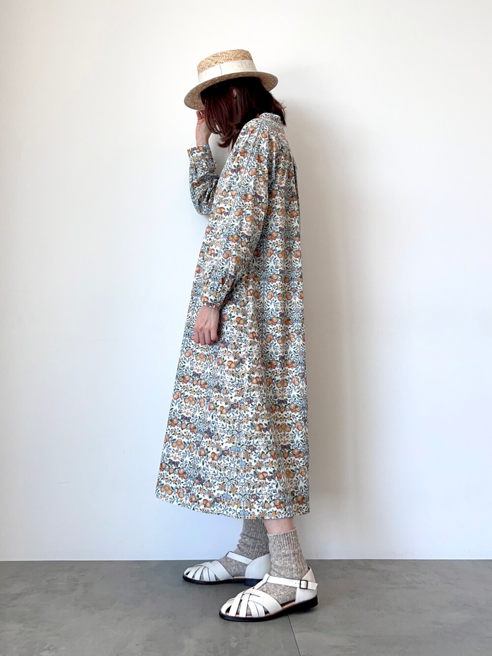 オレンジ系のワンピース、ホワイト系のサンダル、ホワイト系のハットを着用したレディースの春コーディネートの3枚目の写真