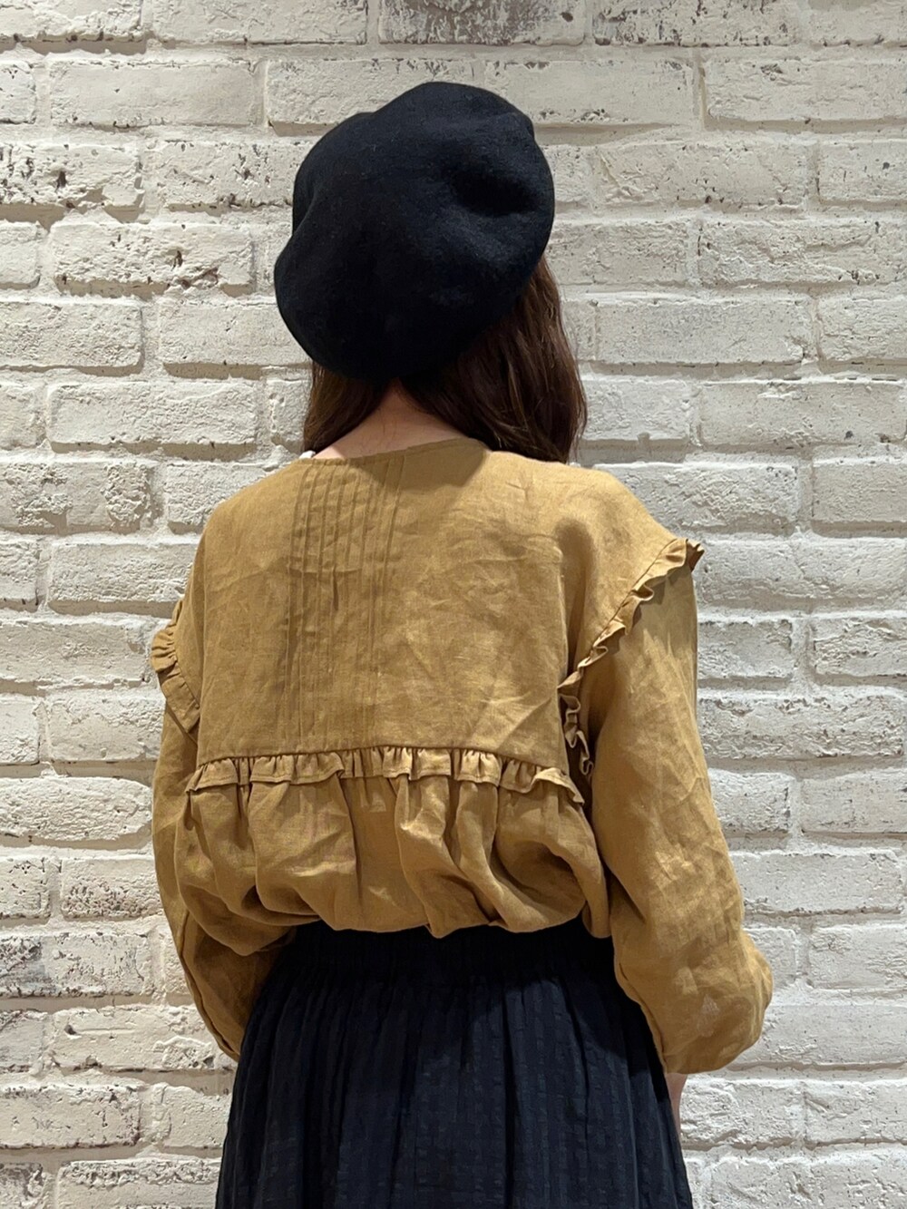 イエロー系のチュニック、ブラック系のスカート、ブラック系のハットを着用したレディースの秋コーディネートの4枚目の写真