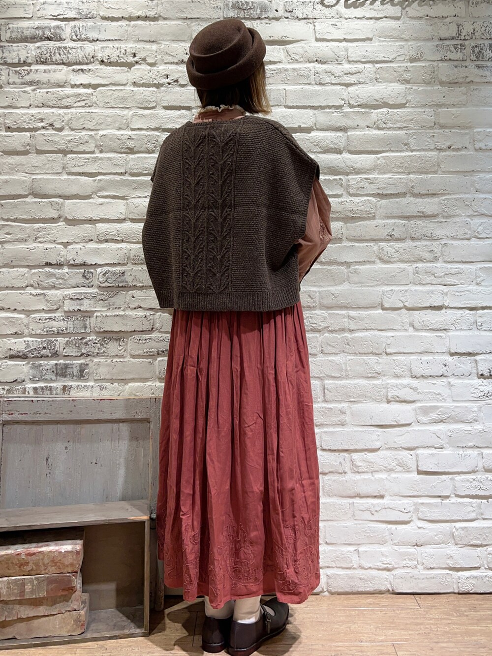 ホワイト系のニット/セーター、ブラウン系のベスト、レッド系のスカートを着用したレディースの秋コーディネートの4枚目の写真