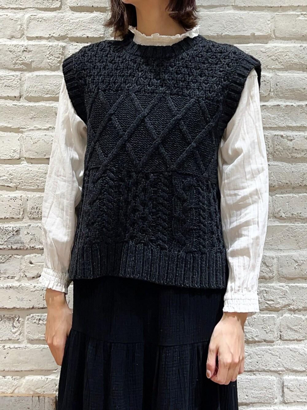 グレー系のベスト、ホワイト系のシャツ/ブラウス、ブラック系のスカートを着用したレディースの冬コーディネートの2枚目の写真