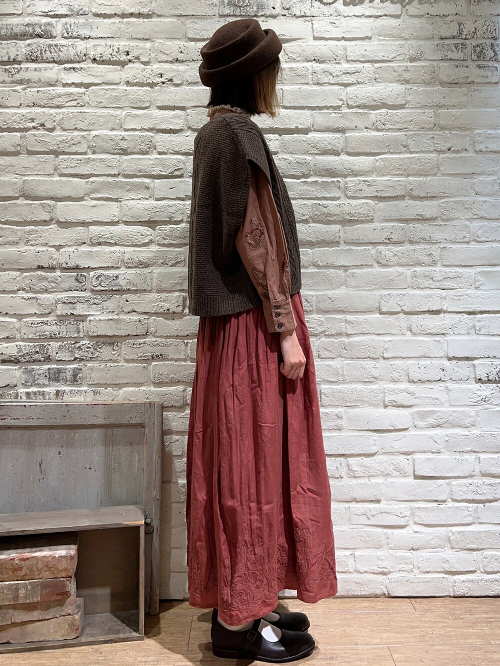 ホワイト系のニット/セーター、ブラウン系のベスト、レッド系のスカートを着用したレディースの秋コーディネートの3枚目の写真