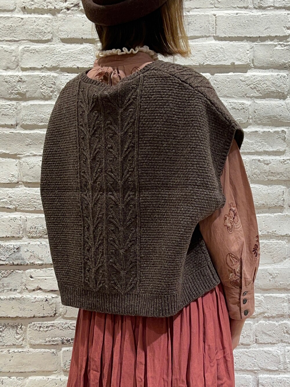 ホワイト系のニット/セーター、ブラウン系のベスト、レッド系のスカートを着用したレディースの秋コーディネートの5枚目の写真