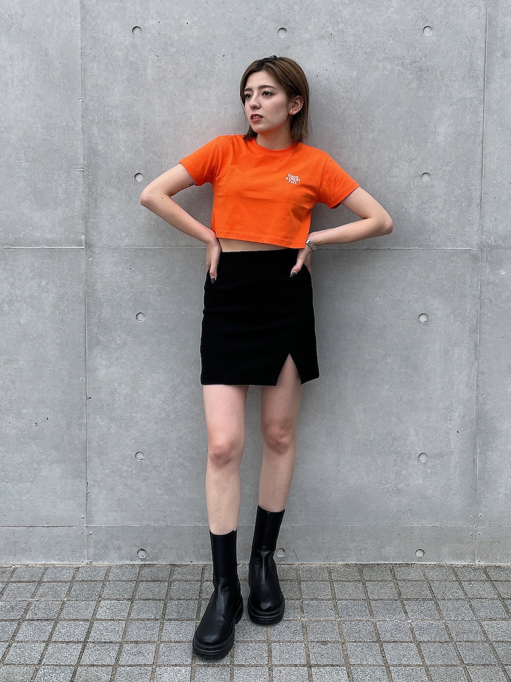 オレンジ系のTシャツ/カットソー、ブラック系のスカート、ブラック系のブーツを着用したレディースの夏コーディネートの2枚目の写真