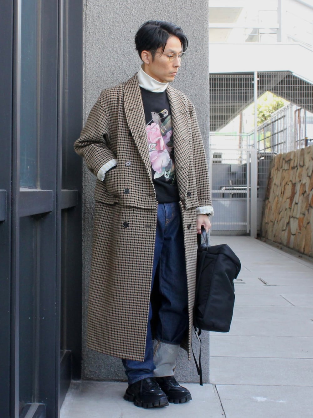 ベージュ系のステンカラーコート、ブラック系のスニーカー、ブルー系のデニムパンツを着用したメンズの冬コーディネートの2枚目の写真