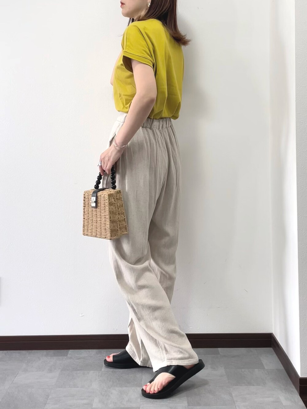 イエロー系のTシャツ/カットソー、ブラウン系のかごバッグ、ベージュ系のスラックスを着用したレディースの夏コーディネートの2枚目の写真