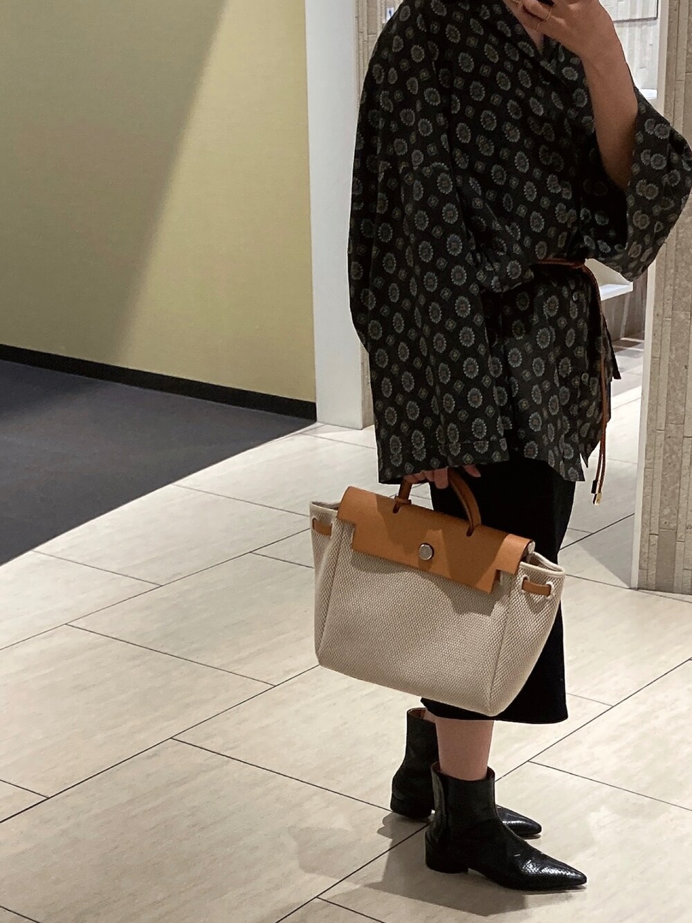 ブラック系のシャツ/ブラウス、ブラック系のブーツ、ベージュ系のバッグを着用したレディースの秋コーディネートの2枚目の写真