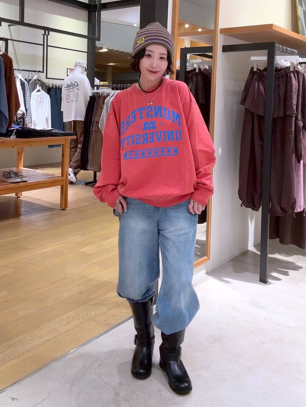 レッド系のスウェット、ブラック系のブーツ、ブルー系のデニムパンツを着用したレディースの秋コーディネートの4枚目の写真