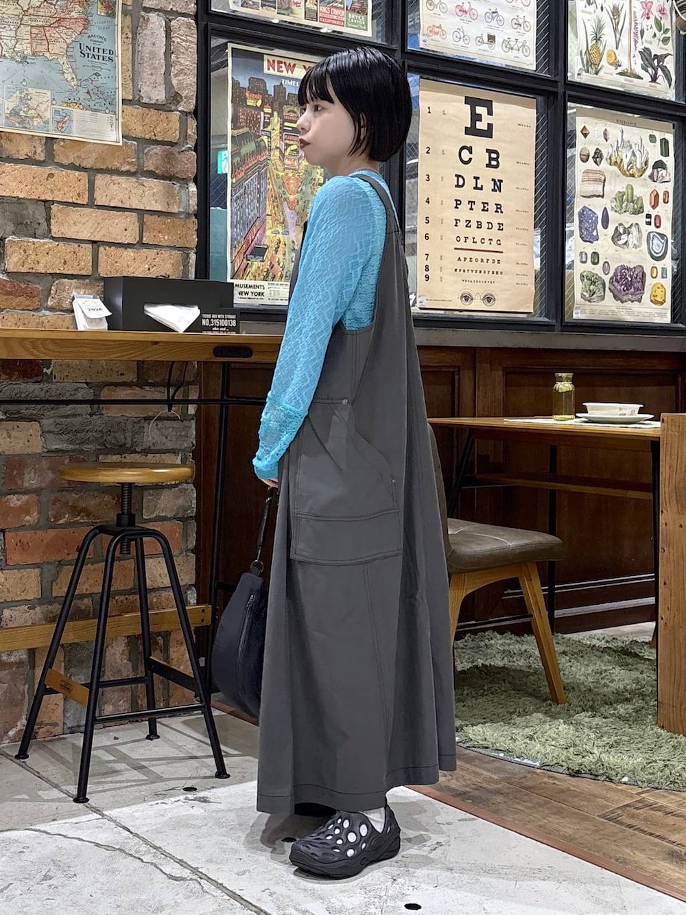 ブラック系のハンドバッグ、ブルー系のTシャツ/カットソー、グレー系のジャンパースカートを着用したレディースの夏コーディネートの2枚目の写真