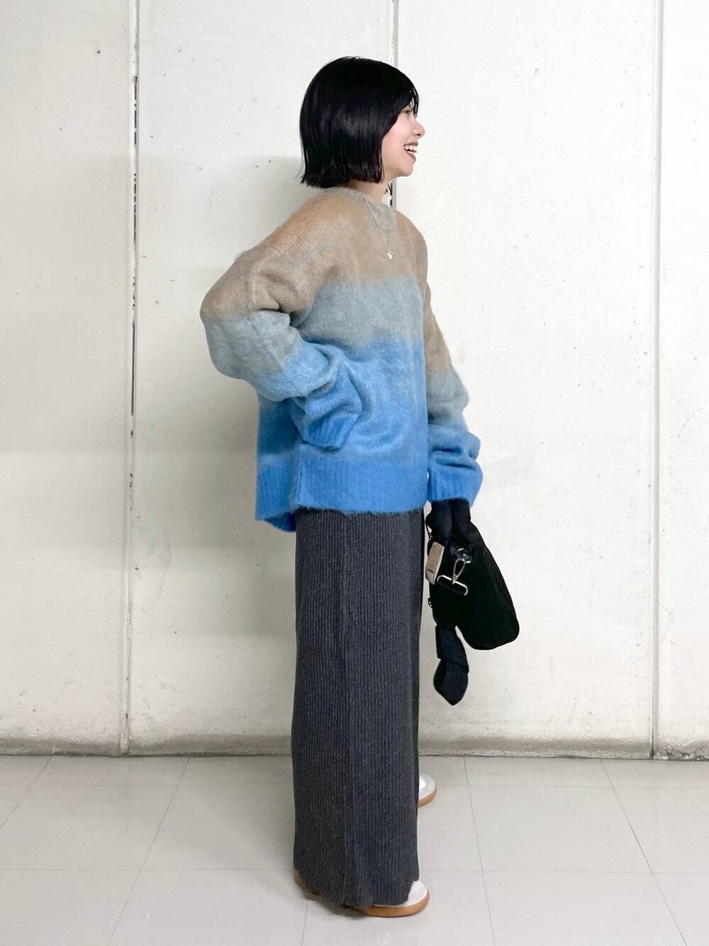 ブラック系のトートバッグ、グレー系のスカート、ブルー系のニット/セーターを着用したレディースの秋コーディネートの2枚目の写真