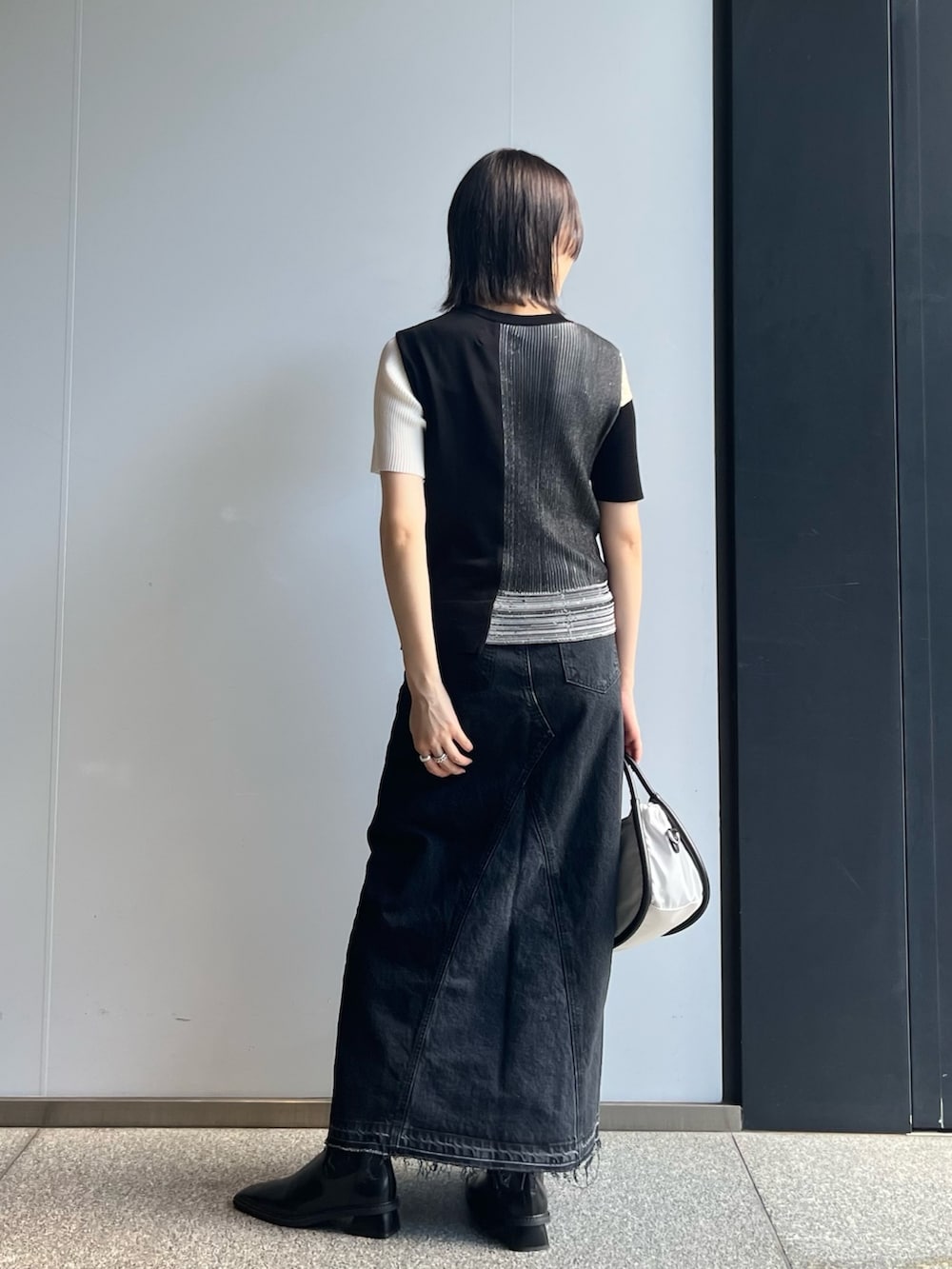 ブラック系のニット/セーター、ブラック系のスカート、ホワイト系のショルダーバッグを着用したレディースの秋コーディネートの4枚目の写真