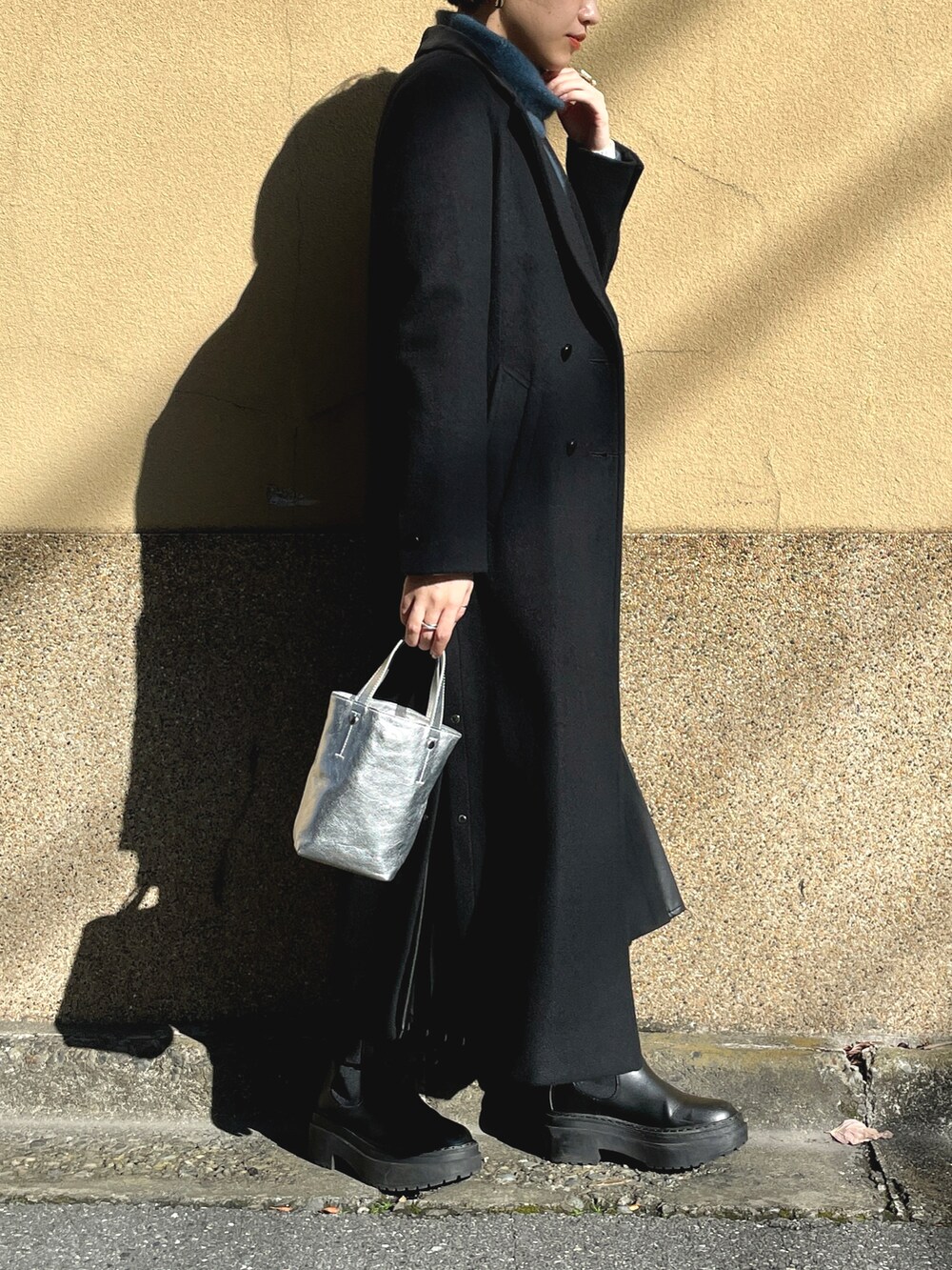 ブラック系のチェスターコート、ブルー系のニット/セーター、ホワイト系のワンピースを着用したレディースの春コーディネートの2枚目の写真