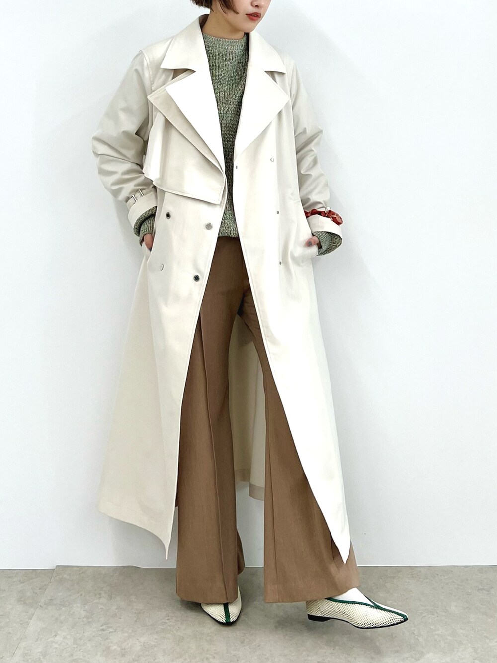 ホワイト系のトレンチコート、グリーン系のニット/セーター、ベージュ系のその他パンツを着用したレディースの冬コーディネートの2枚目の写真