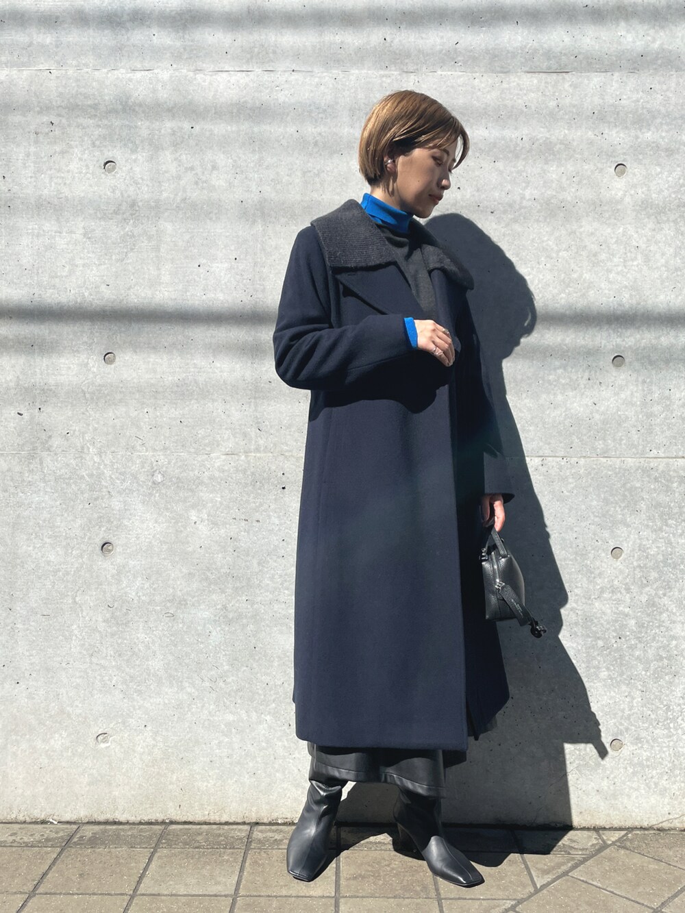 ブルー系のチェスターコート、グレー系のニット/セーター、ブラック系のショルダーバッグを着用したレディースの春コーディネートの2枚目の写真