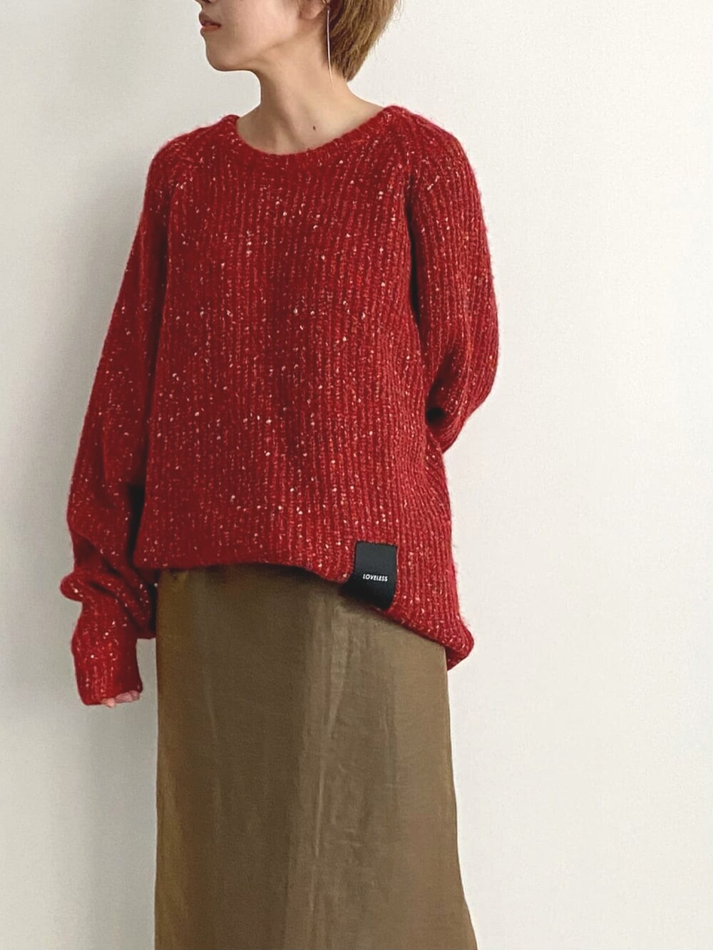 レッド系のニット/セーター、ブラウン系のスカート、ベージュ系のブーツを着用したレディースの冬コーディネートの2枚目の写真