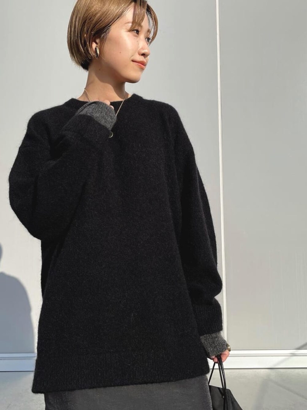 ブラック系のニット/セーター、ブラック系のハンドバッグ、ブラック系のスカートを着用したレディースの春コーディネートの2枚目の写真