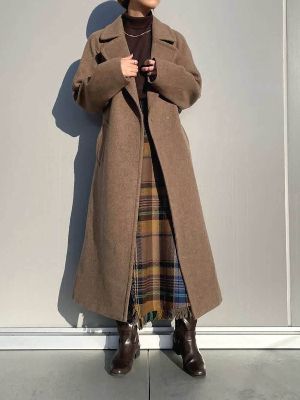 ブラウン系のチェスターコート、ブラウン系のニット/セーター、ブルー系のスカートを着用したレディースの春コーディネートの2枚目の写真