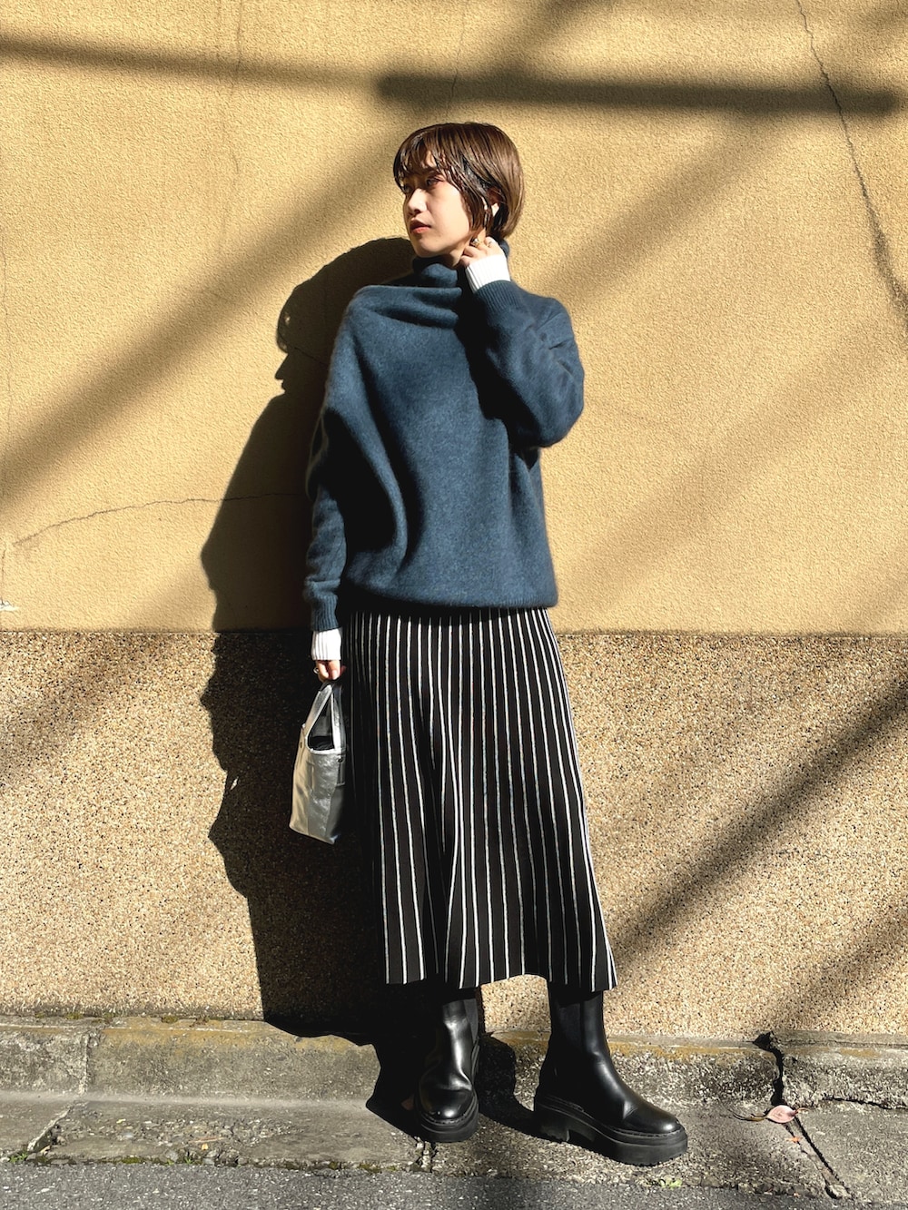 ブラック系のチェスターコート、ブルー系のニット/セーター、ホワイト系のワンピースを着用したレディースの春コーディネートの4枚目の写真