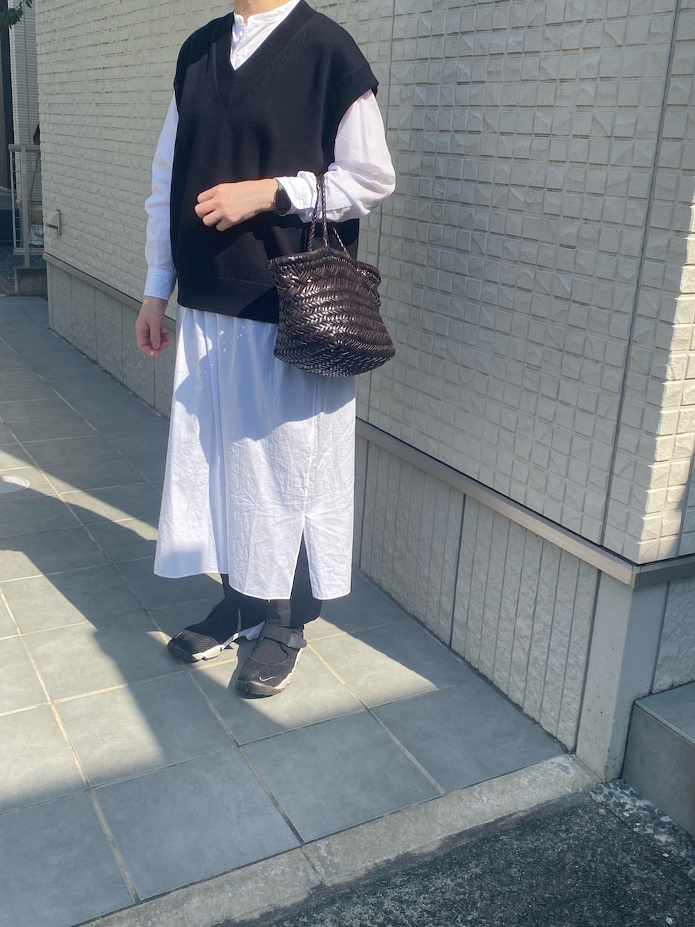 ブラック系のベスト、ホワイト系のシャツワンピースを着用したレディースの春コーディネートの2枚目の写真