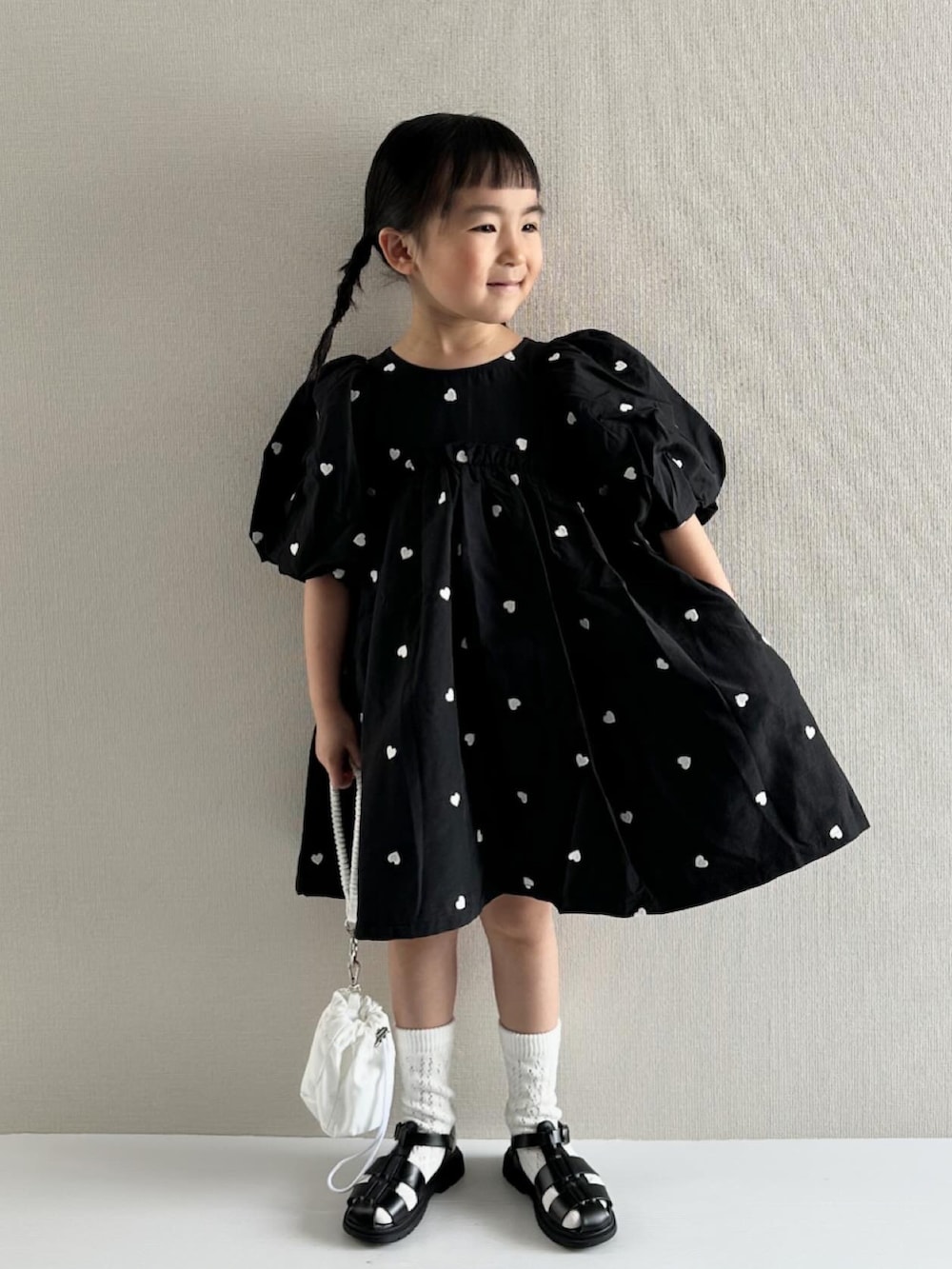 ブラック系のワンピース、ホワイト系のショルダーバッグ、ブラック系のサンダルを着用したキッズの春コーディネートの4枚目の写真