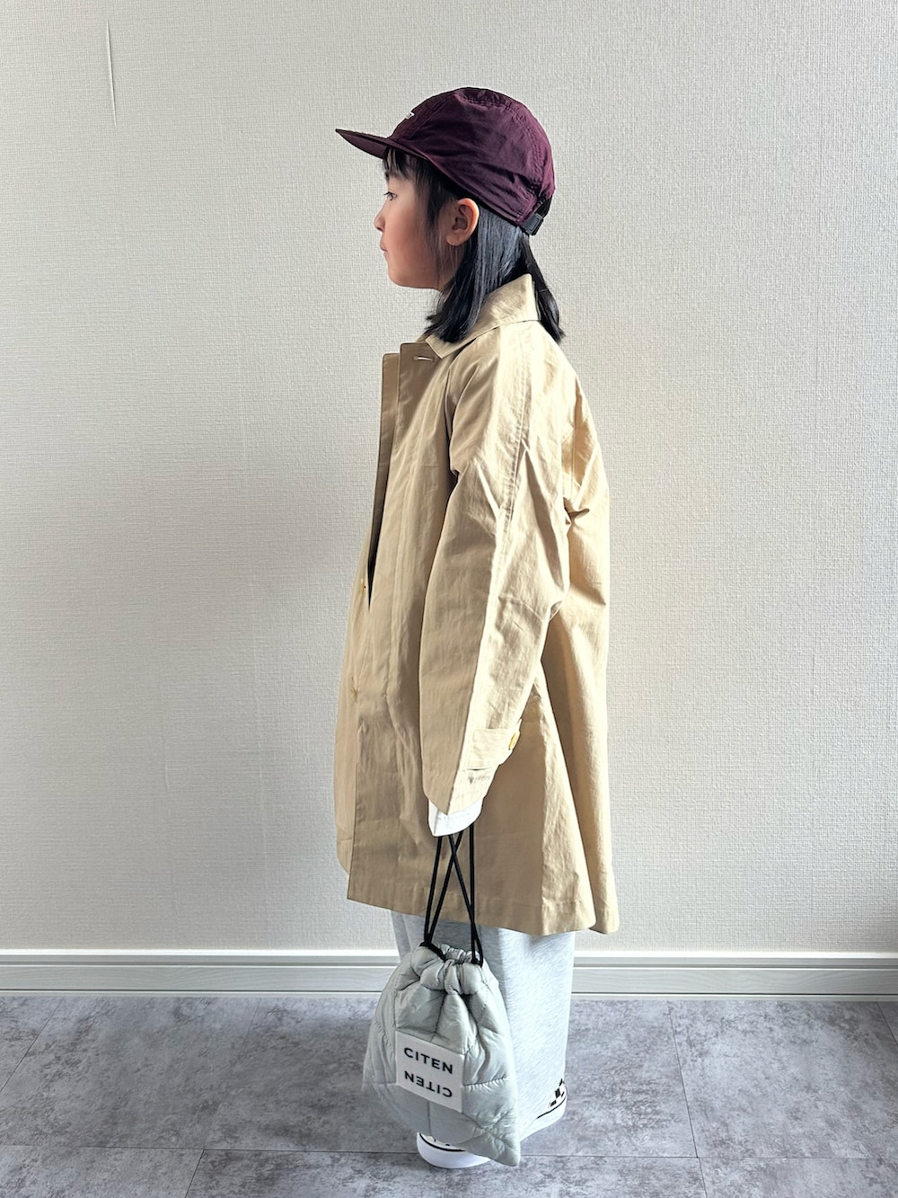 ベージュ系のステンカラーコート、ベージュ系のTシャツ/カットソー、グレー系のスウェットパンツを着用したキッズの春コーディネートの2枚目の写真