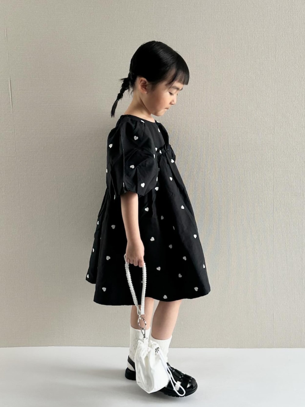 ブラック系のワンピース、ホワイト系のショルダーバッグ、ブラック系のサンダルを着用したキッズの春コーディネートの2枚目の写真