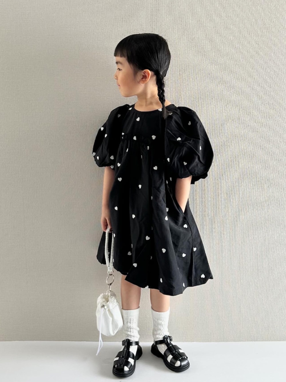 ブラック系のワンピース、ホワイト系のショルダーバッグ、ブラック系のサンダルを着用したキッズの春コーディネートの3枚目の写真