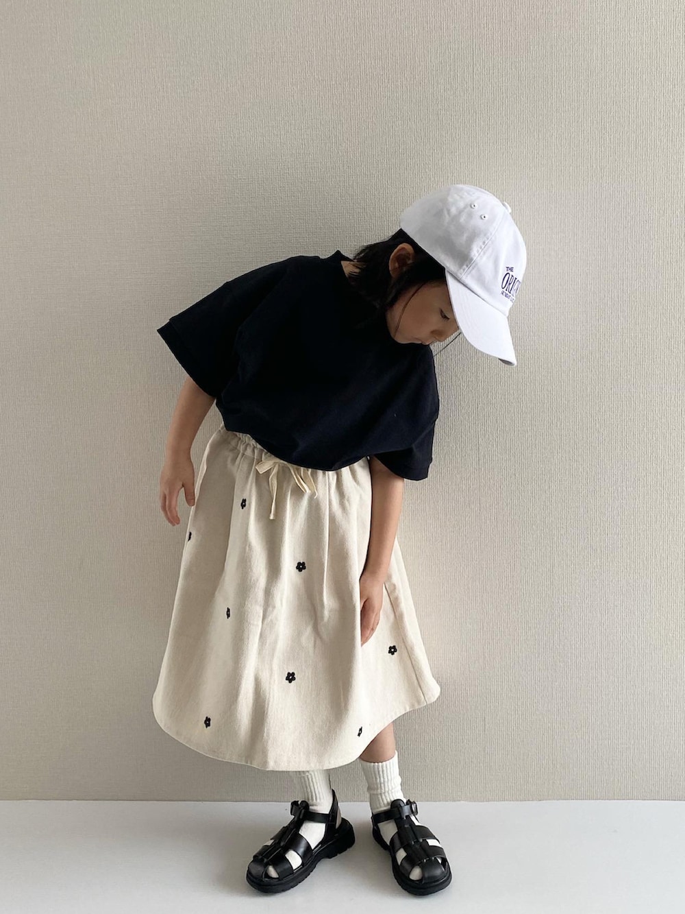 ブラック系のTシャツ/カットソー、ホワイト系のスカート、ブラック系のサンダルを着用したキッズの冬コーディネートの4枚目の写真