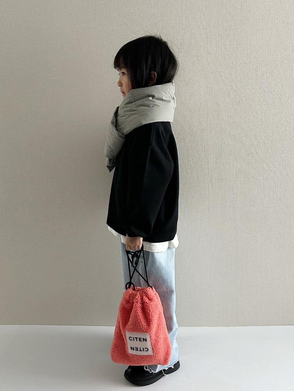 ブラック系のニット/セーター、ブルー系のデニムパンツ、オレンジ系のショルダーバッグを着用したキッズの秋コーディネートの2枚目の写真