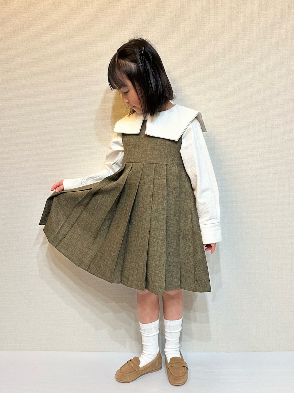 ブラウン系のジャンパースカート、ホワイト系のシャツ/ブラウス、ブラウン系のローファーを着用したキッズの冬コーディネートの5枚目の写真