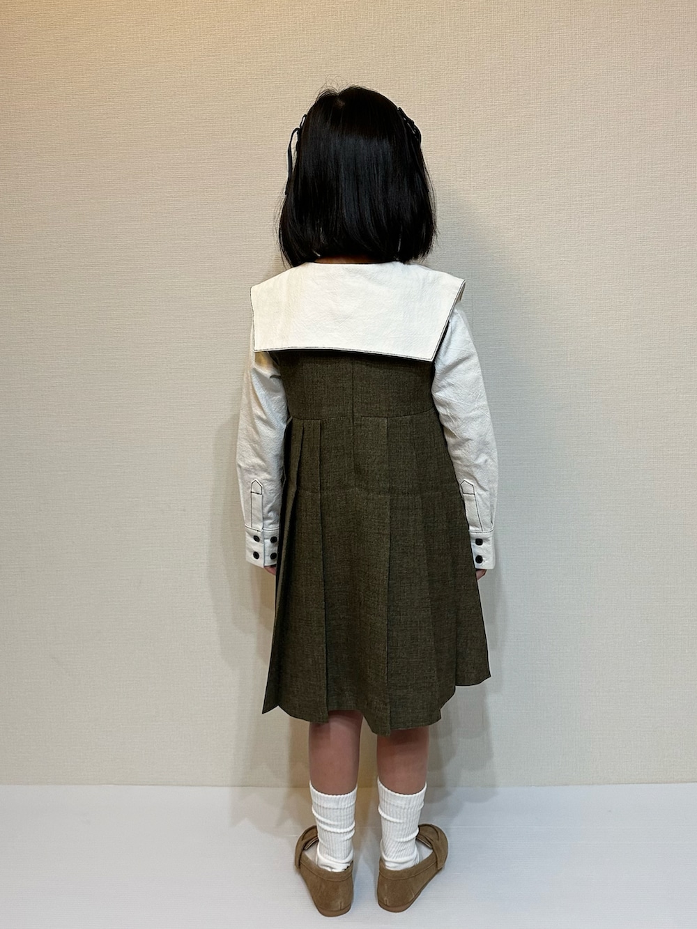 ブラウン系のジャンパースカート、ホワイト系のシャツ/ブラウス、ブラウン系のローファーを着用したキッズの冬コーディネートの3枚目の写真