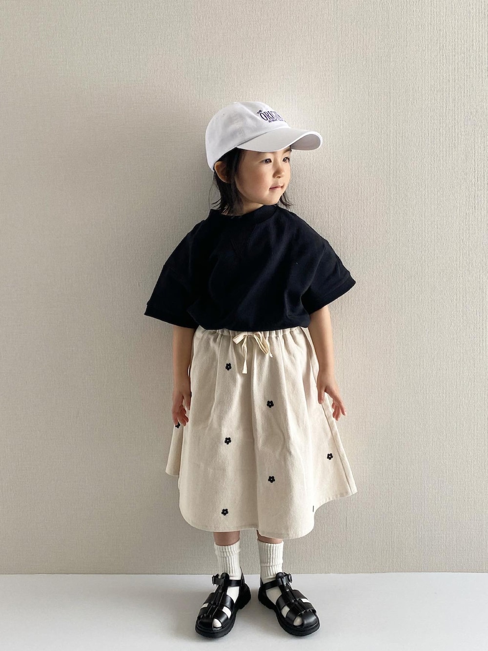 ブラック系のTシャツ/カットソー、ホワイト系のスカート、ブラック系のサンダルを着用したキッズの冬コーディネートの2枚目の写真