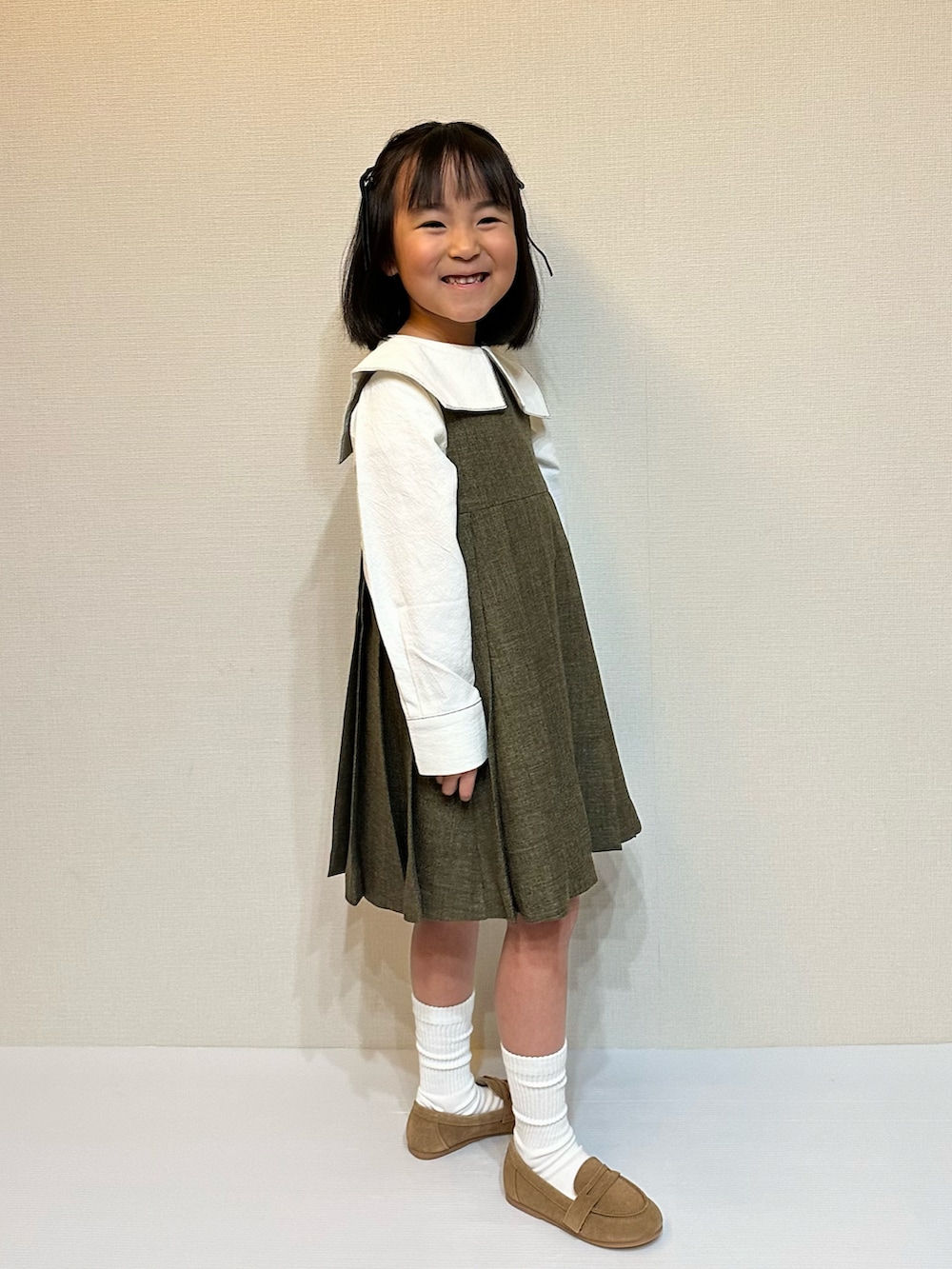 ブラウン系のジャンパースカート、ホワイト系のシャツ/ブラウス、ブラウン系のローファーを着用したキッズの冬コーディネートの4枚目の写真