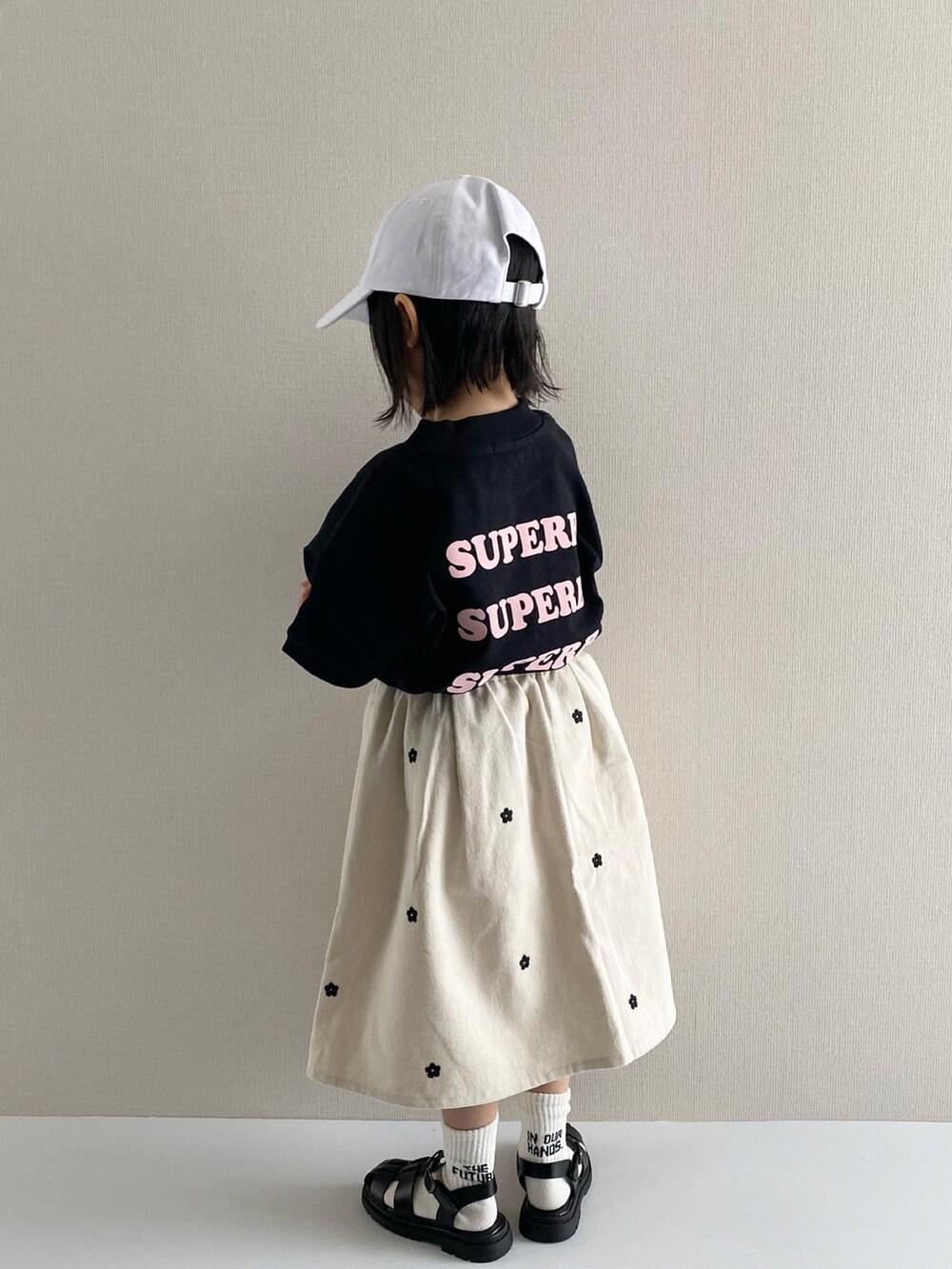 ブラック系のTシャツ/カットソー、ホワイト系のスカート、ブラック系のサンダルを着用したキッズの冬コーディネートの3枚目の写真