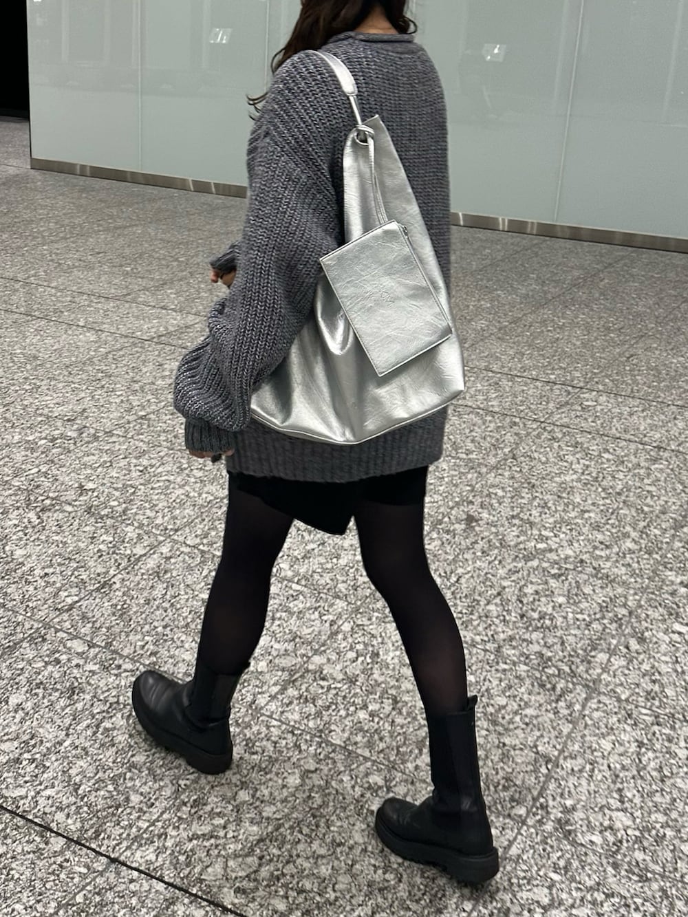 シルバー系のトートバッグ、ブラック系のブーツ、ブルー系のニット/セーターを着用したレディースの秋コーディネートの2枚目の写真