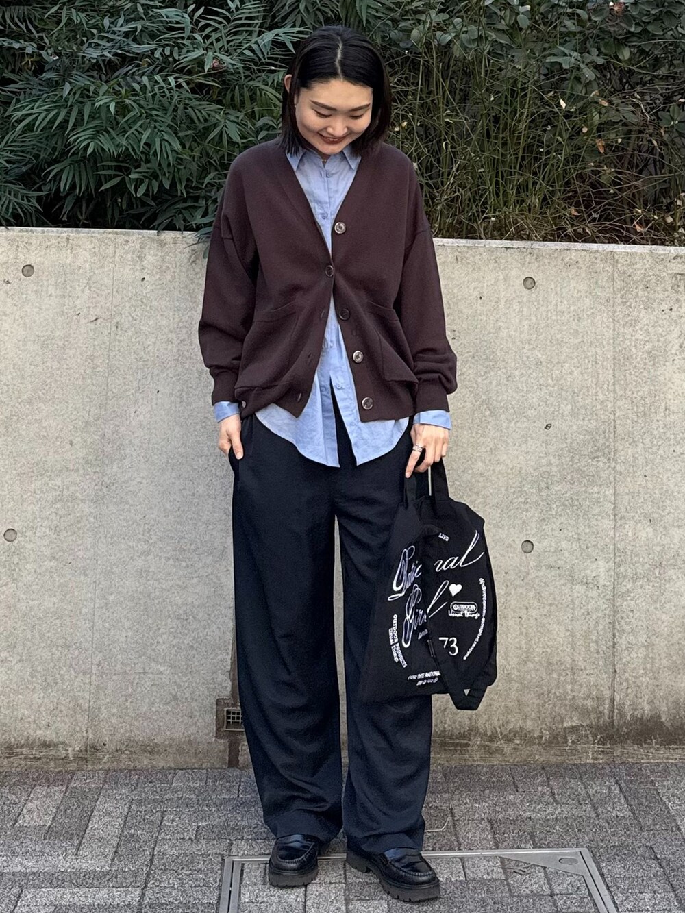 ブルー系のスラックス、ブラウン系のカーディガン/ボレロ、ブラック系のクラッチバッグを着用したレディースの冬コーディネートの2枚目の写真
