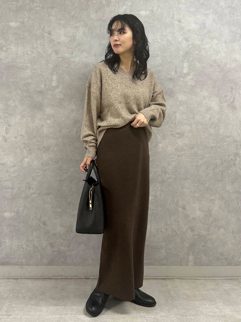 ブラウン系のスカート、ベージュ系のニット/セーター、ブラック系のトートバッグを着用したレディースの冬コーディネートの2枚目の写真