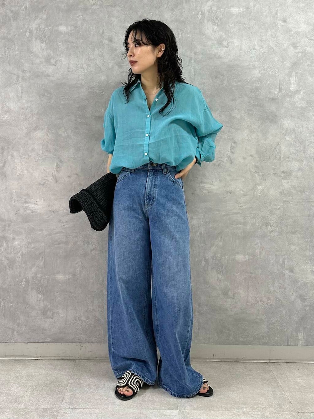 ブラック系のトートバッグ、ブルー系のデニムパンツ、ブラック系のサンダルを着用したレディースの夏コーディネートの2枚目の写真