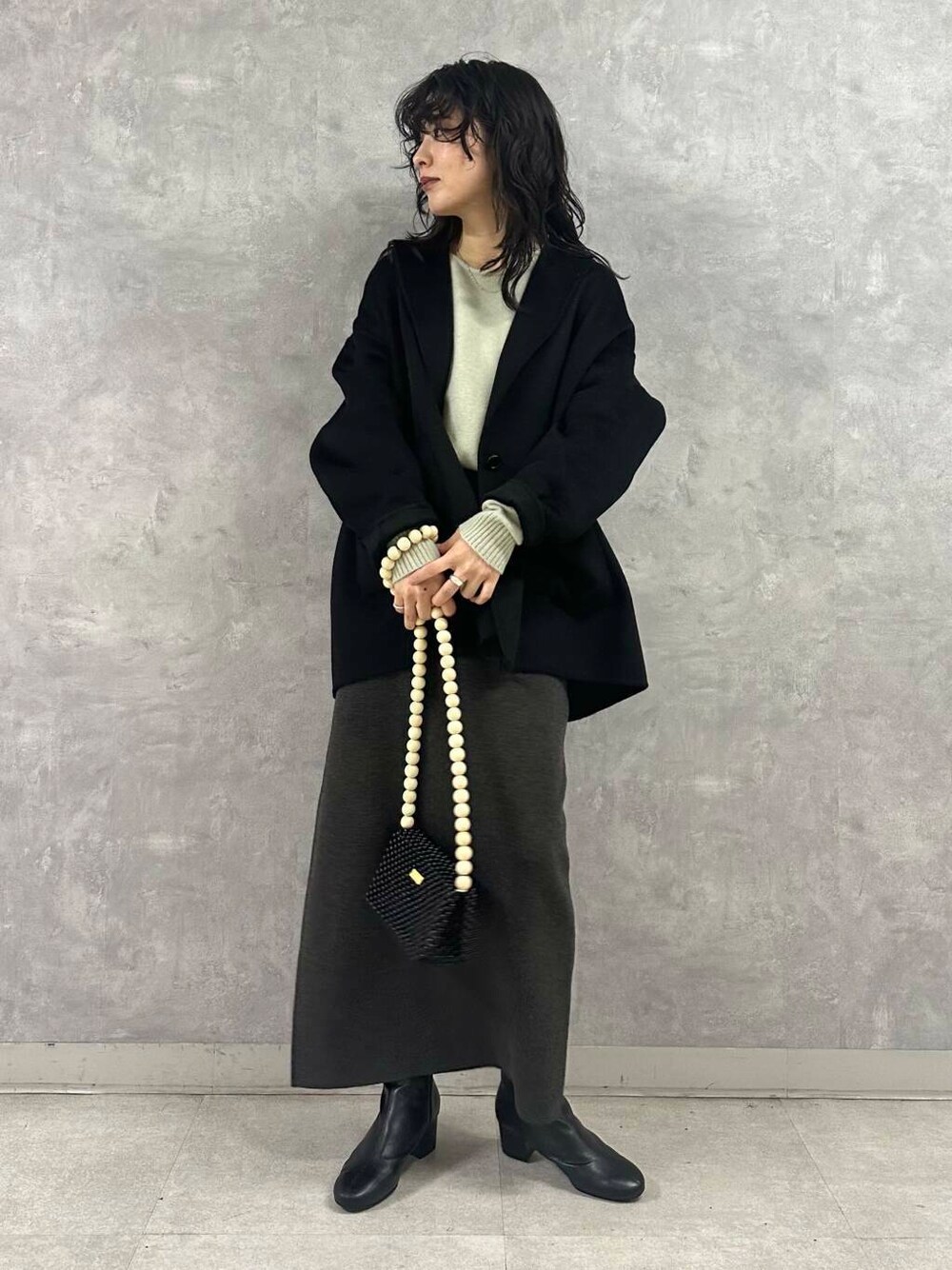 ブラック系のその他アウター、グレー系のスカート、グリーン系のニット/セーターを着用したレディースの冬コーディネートの2枚目の写真