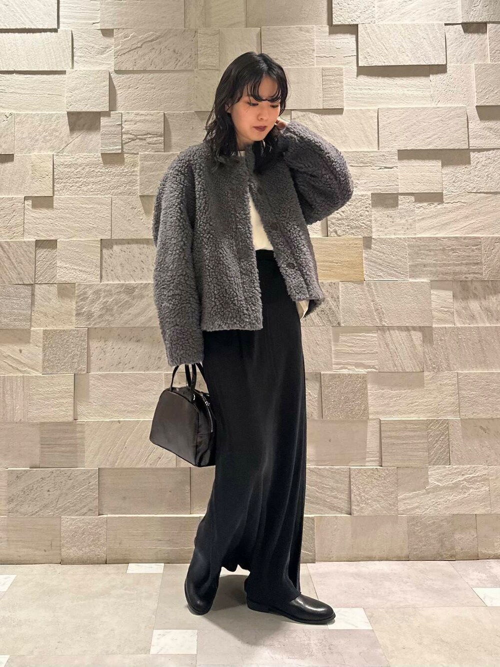 ブラック系のブーツ、ブラック系のショルダーバッグ、ブラック系のスカートを着用したレディースの冬コーディネートの2枚目の写真