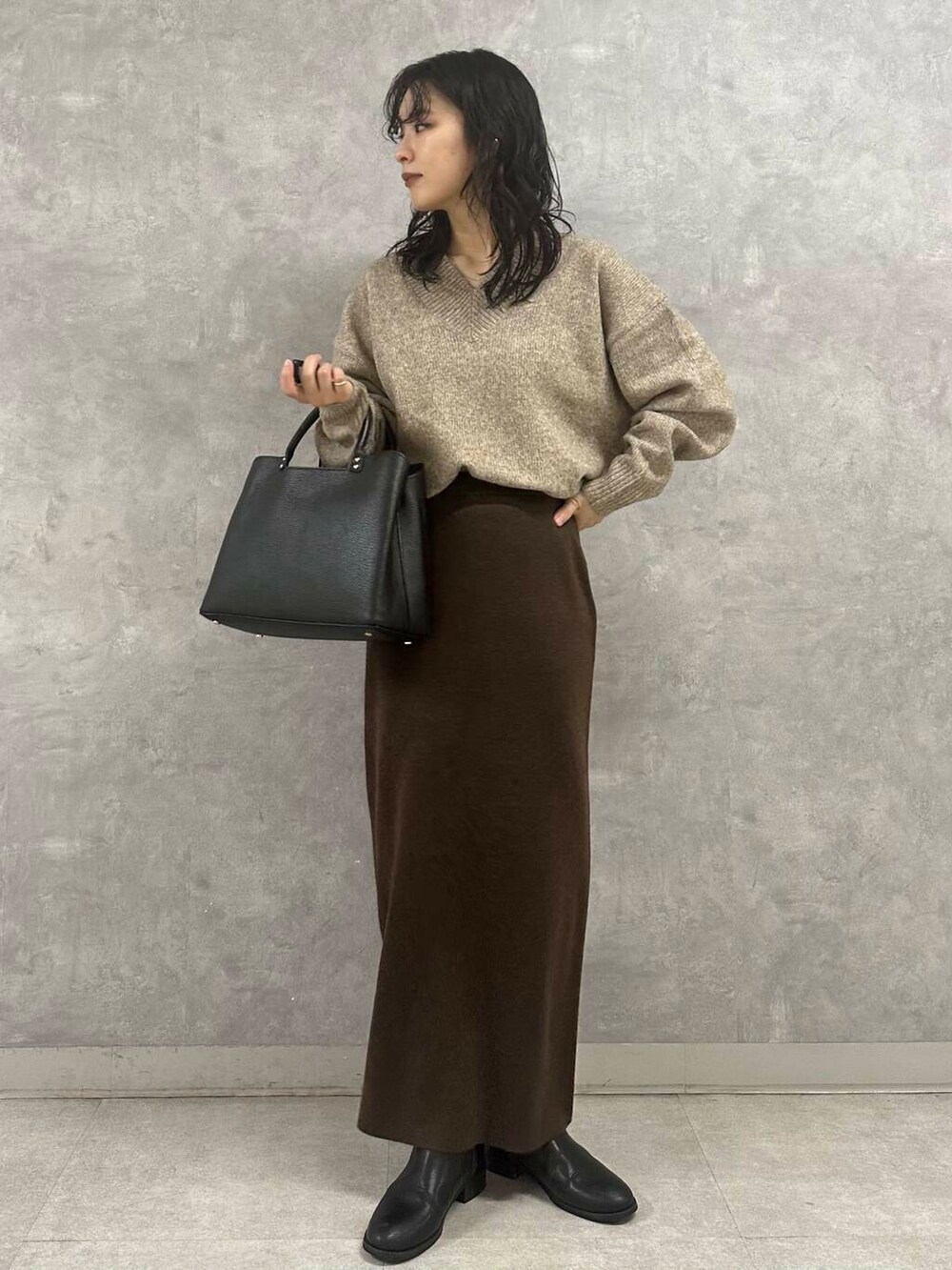 ブラウン系のスカート、ベージュ系のニット/セーター、ブラック系のトートバッグを着用したレディースの冬コーディネートの5枚目の写真