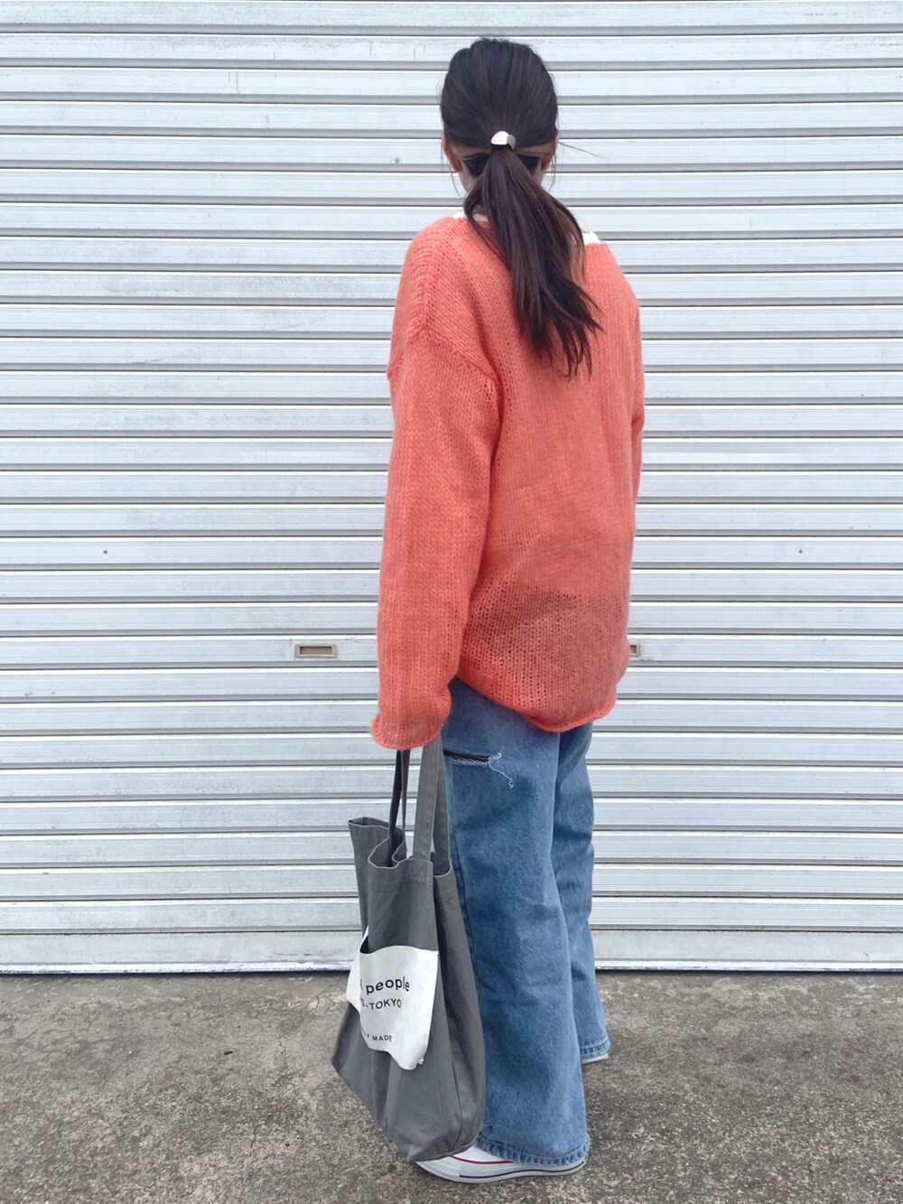 オレンジ系のニット/セーター、ホワイト系のTシャツ/カットソー、ブルー系のデニムパンツを着用したレディースの春コーディネートの2枚目の写真