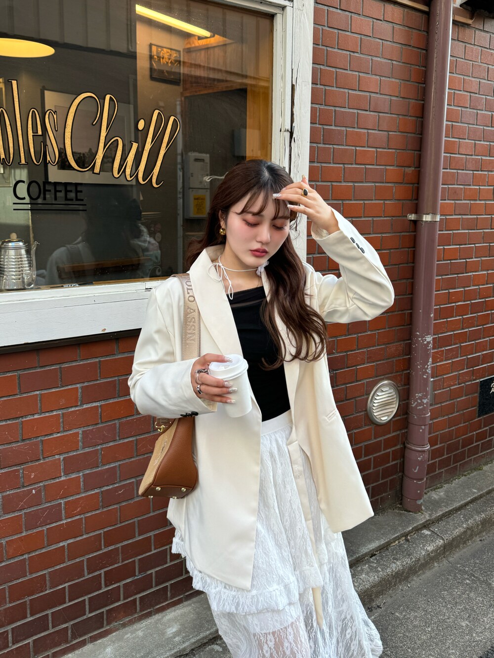 ブラウン系のショルダーバッグ、ホワイト系のスカート、ベージュ系のスニーカーを着用したレディースの春コーディネートの2枚目の写真