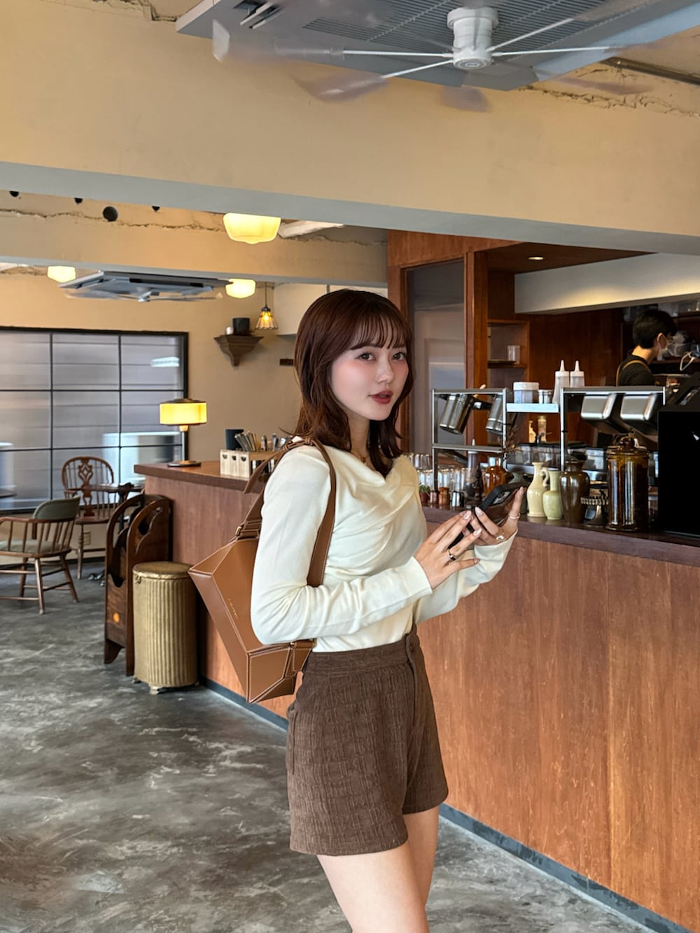 ブラウン系のブーツ、ブラウン系のショルダーバッグ、ベージュ系のカバーオールを着用したレディースの冬コーディネートの2枚目の写真