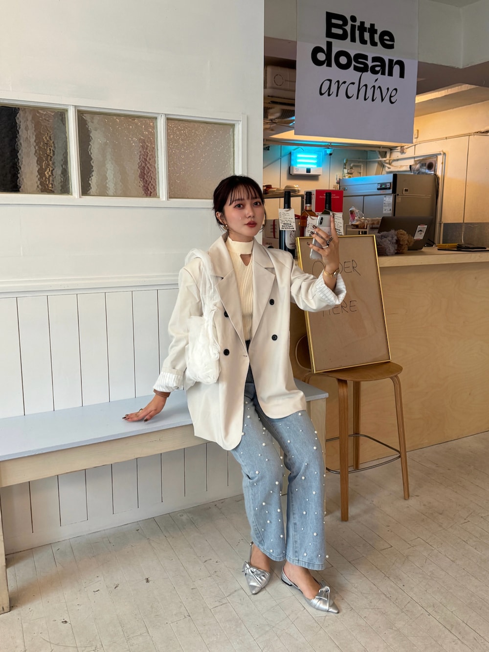 ホワイト系のテーラードジャケット、ブルー系のデニムパンツ、ホワイト系のハンドバッグを着用したレディースの秋コーディネートの3枚目の写真