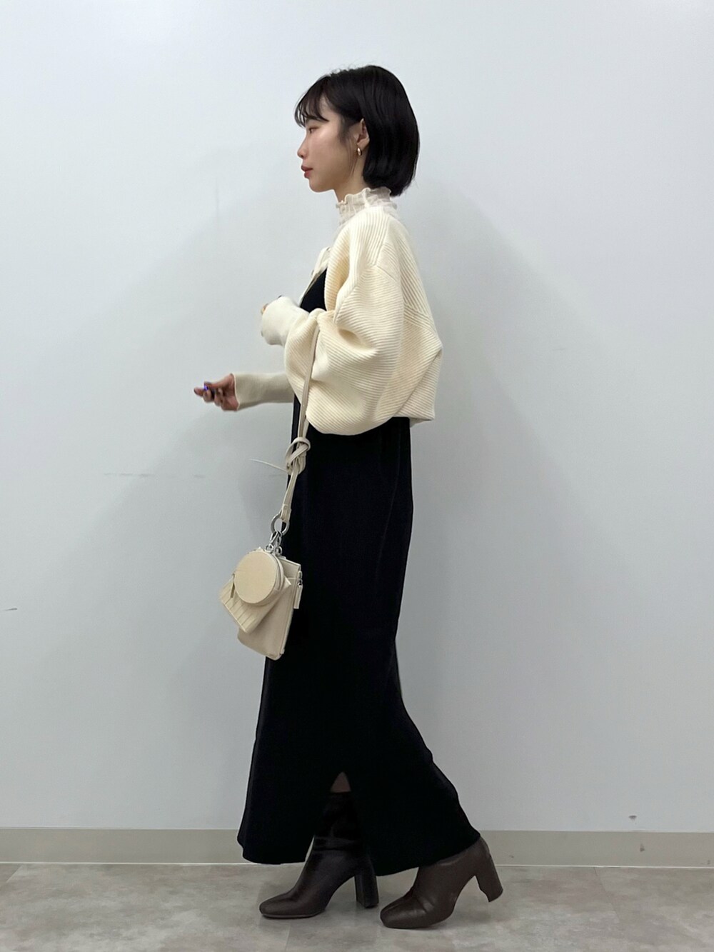 ブラック系のワンピース、ホワイト系のショルダーバッグ、ブラウン系のブーツを着用したレディースの冬コーディネートの2枚目の写真