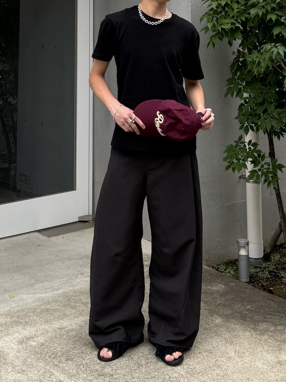 ブラック系のTシャツ/カットソー、グレー系のスラックス、ブラック系のサンダルを着用したメンズの夏コーディネートの3枚目の写真