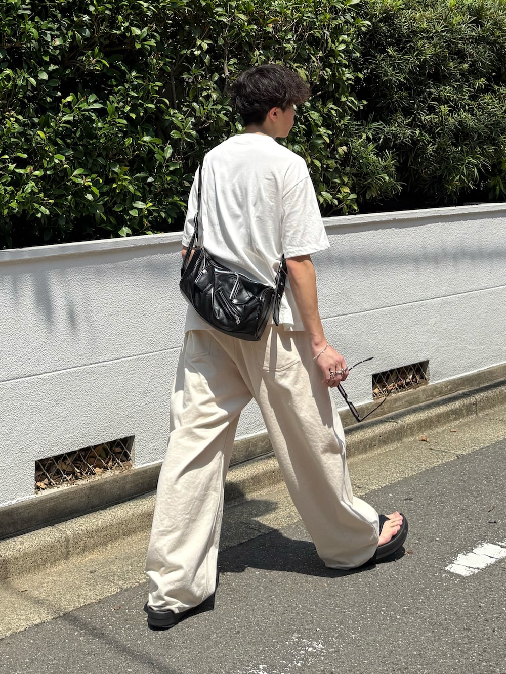 ホワイト系のTシャツ/カットソー、ブラック系のショルダーバッグ、ホワイト系のデニムパンツを着用したメンズの夏コーディネートの2枚目の写真