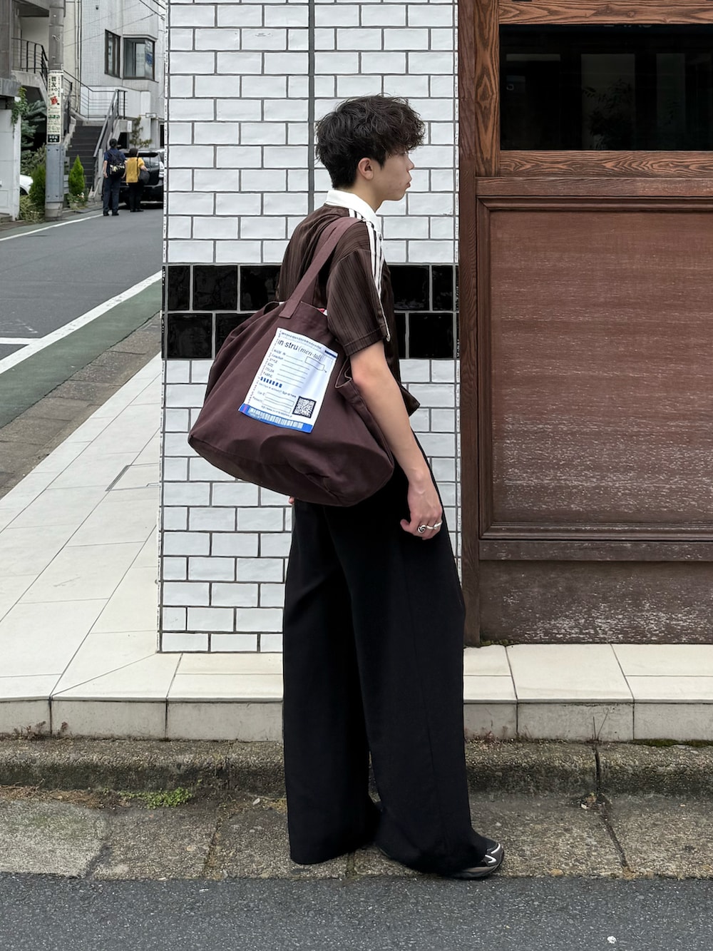ブラウン系のTシャツ/カットソー、ブラック系のスラックス、ブラウン系のトートバッグを着用したメンズの夏コーディネートの2枚目の写真