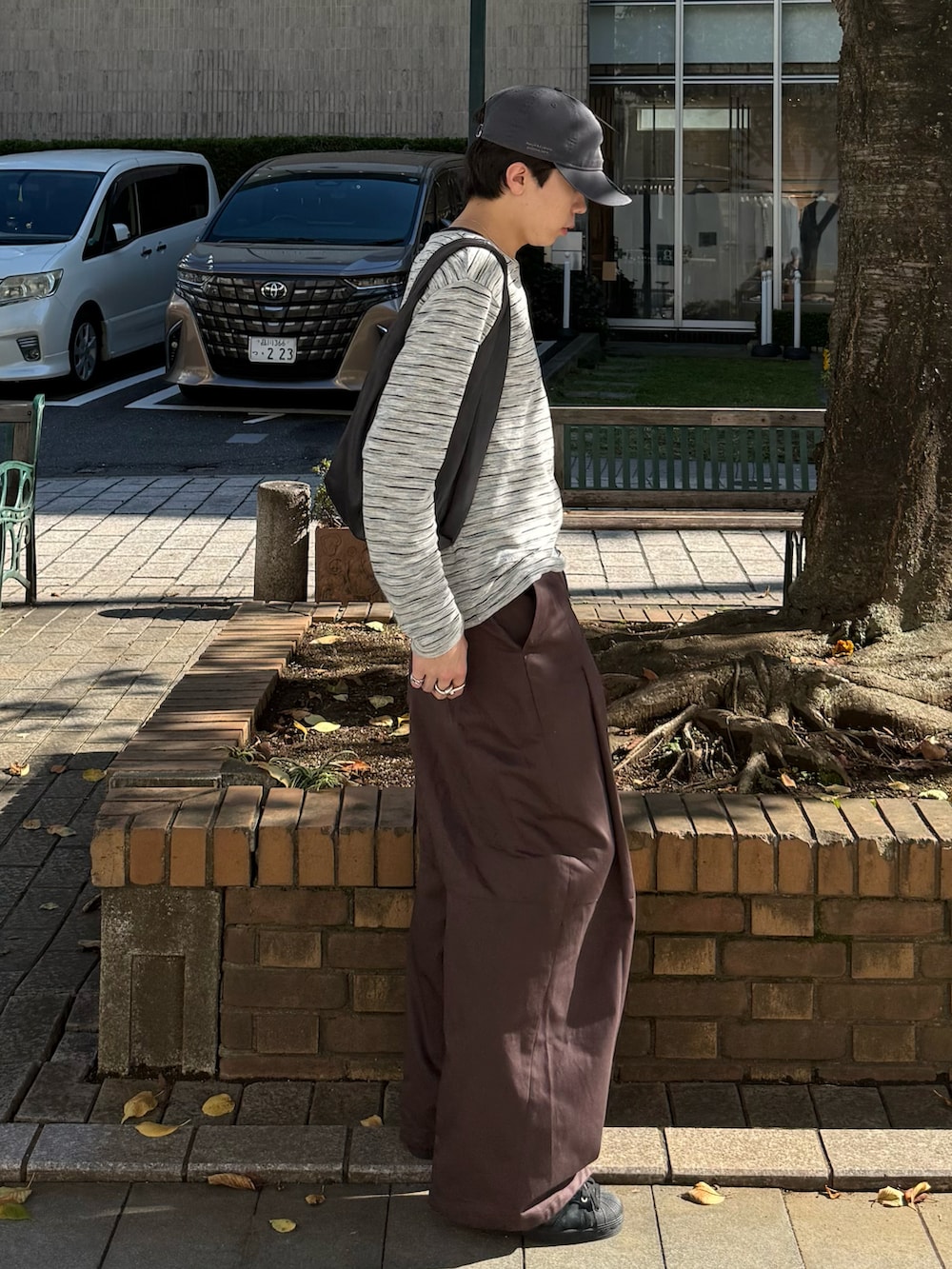 グレー系のTシャツ/カットソー、ブラウン系のその他パンツ、グレー系のハンドバッグを着用したメンズの秋コーディネートの2枚目の写真