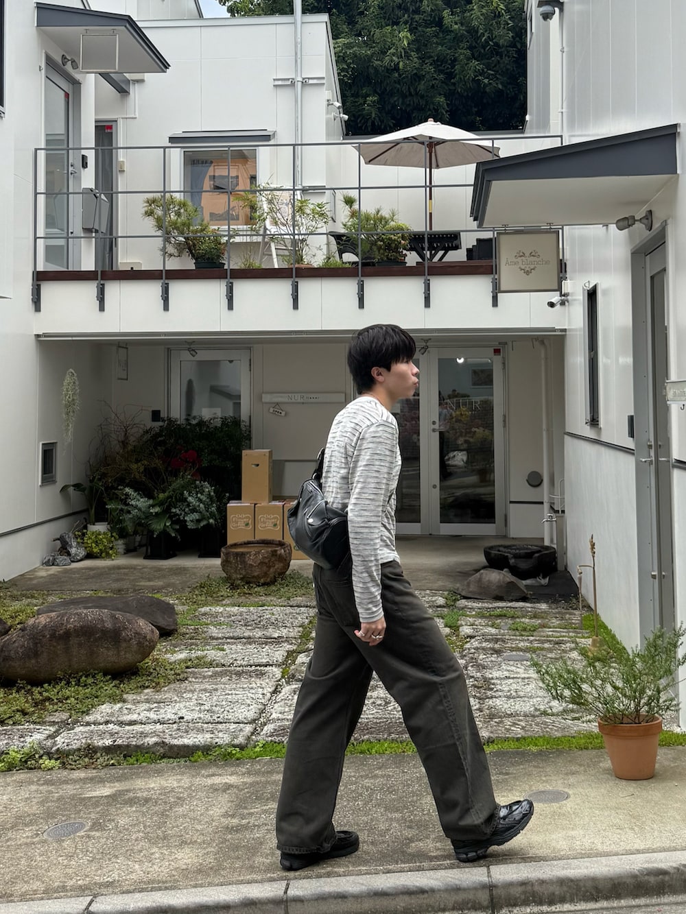 グレー系のTシャツ/カットソー、ブラウン系のデニムパンツ、ブラック系のショルダーバッグを着用したメンズの秋コーディネートの3枚目の写真